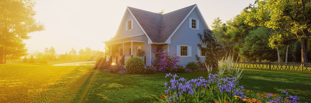 A simple home with a covered porch in a lush green yard at sunset