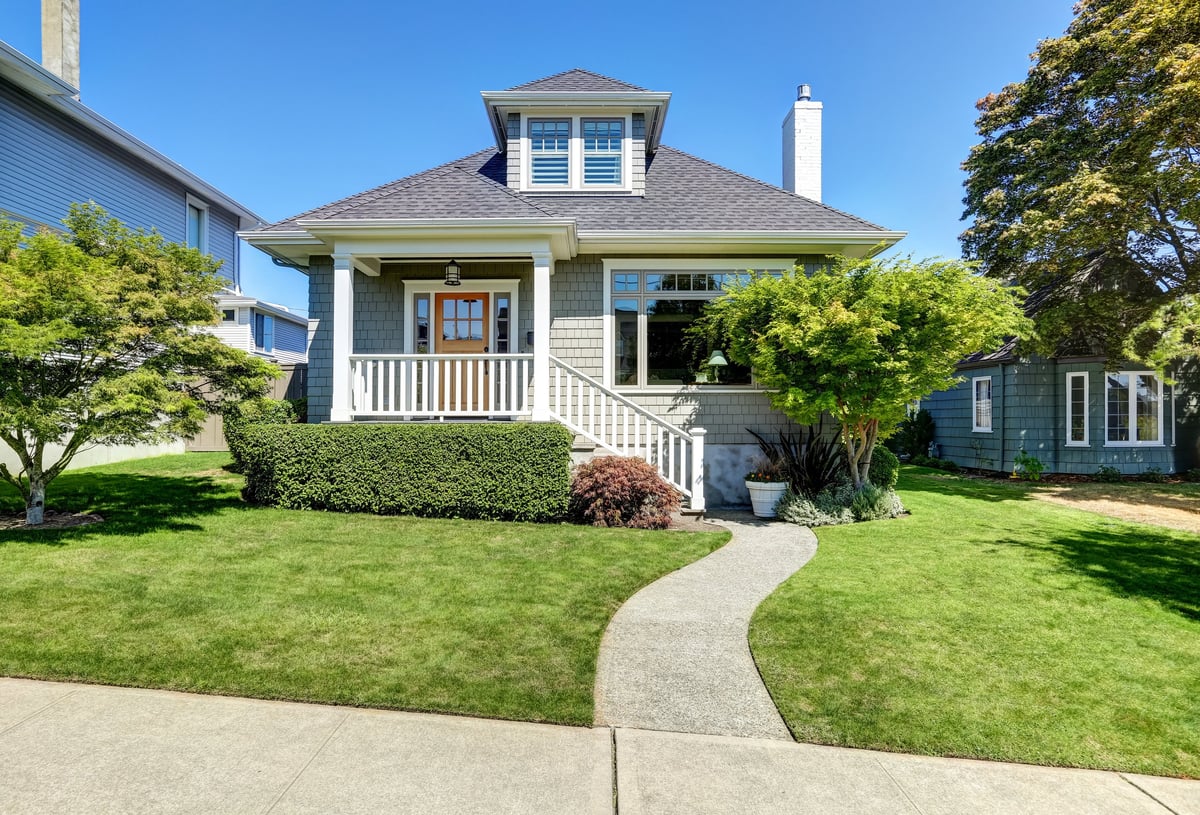A single-family craftsman home with neatly trimmed front yard under a blue sky